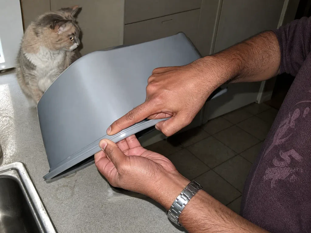 Hands checking the molded rim seam of a cheap plastic litter box for sharp flashing before buying