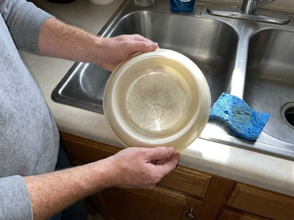 Close view of a scratched plastic cat bowl interior held over a kitchen sink under harsh flash
