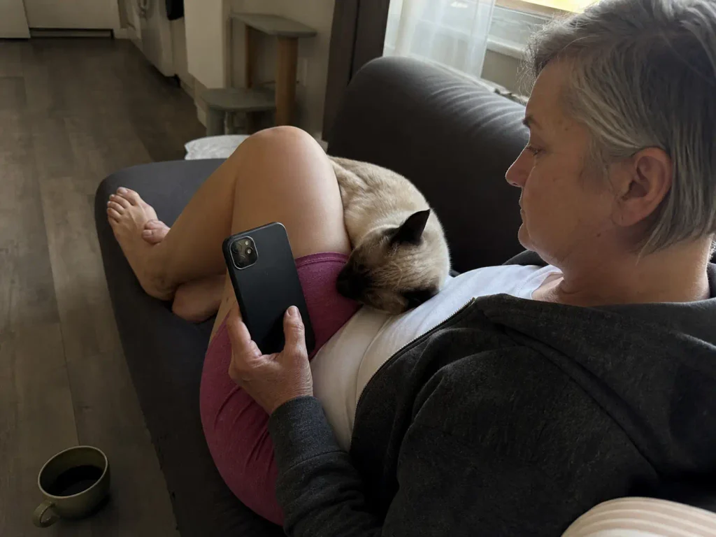 Woman checking a litter box usage app on her phone from the sofa with a cat beside her