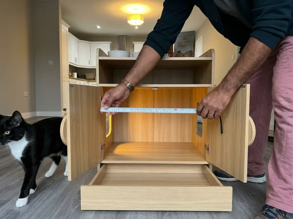 Tape measure stretched across the inside of a natural wood litter box cabinet with the drawer pulled out