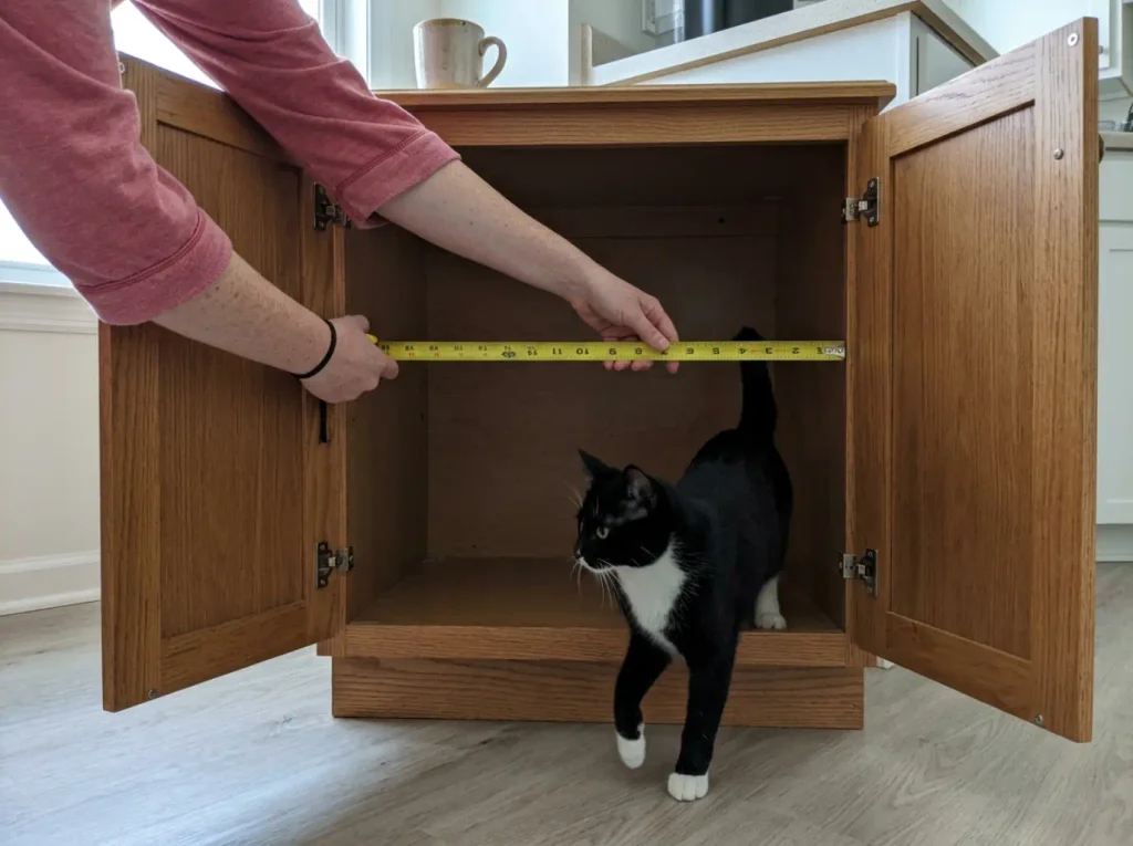 Tape measure held inside an open litter box cabinet showing the interior is narrower than the listing