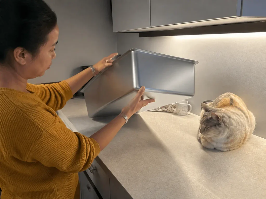Hands turning a stainless steel litter box on a kitchen counter to check the grade stamp on the underside