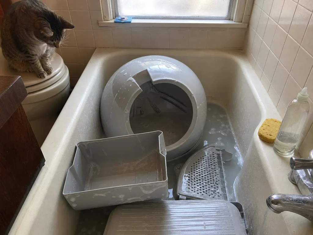 Washable litter box parts laid on a towel in a bathtub with warm soapy water