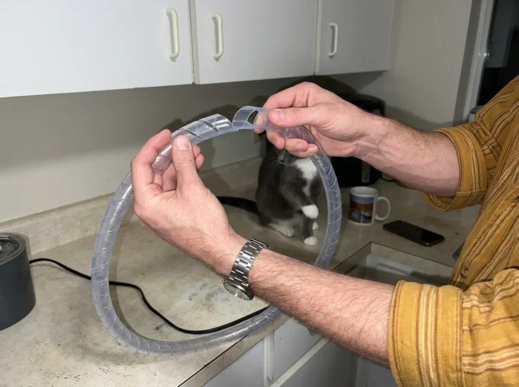 Hands holding a Chewsafe anti-chew cord cover beside a cat water fountain cord
