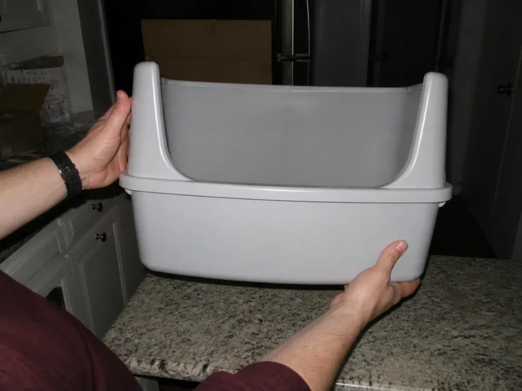 Hands turning a high sided litter box to show the one-piece molded wall with no seam