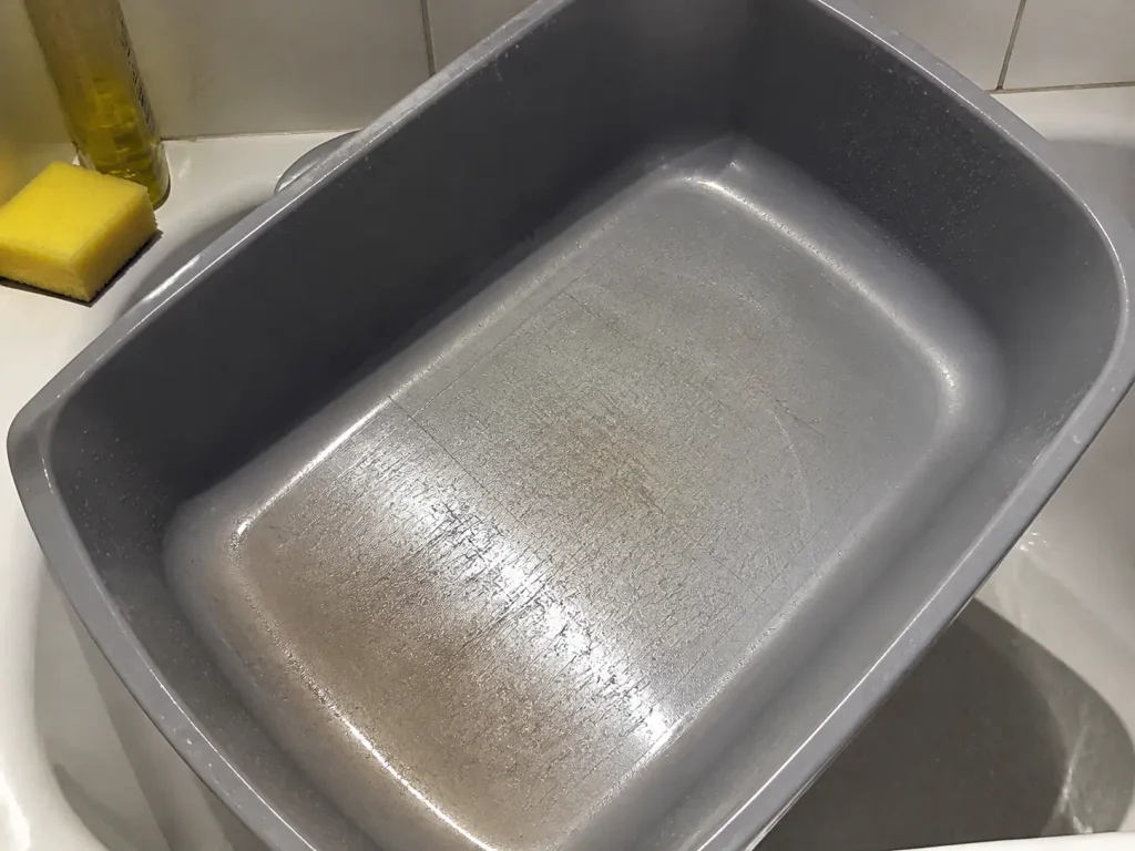 Close-up of a scratched plastic litter box just after washing, still wet on the bathtub edge