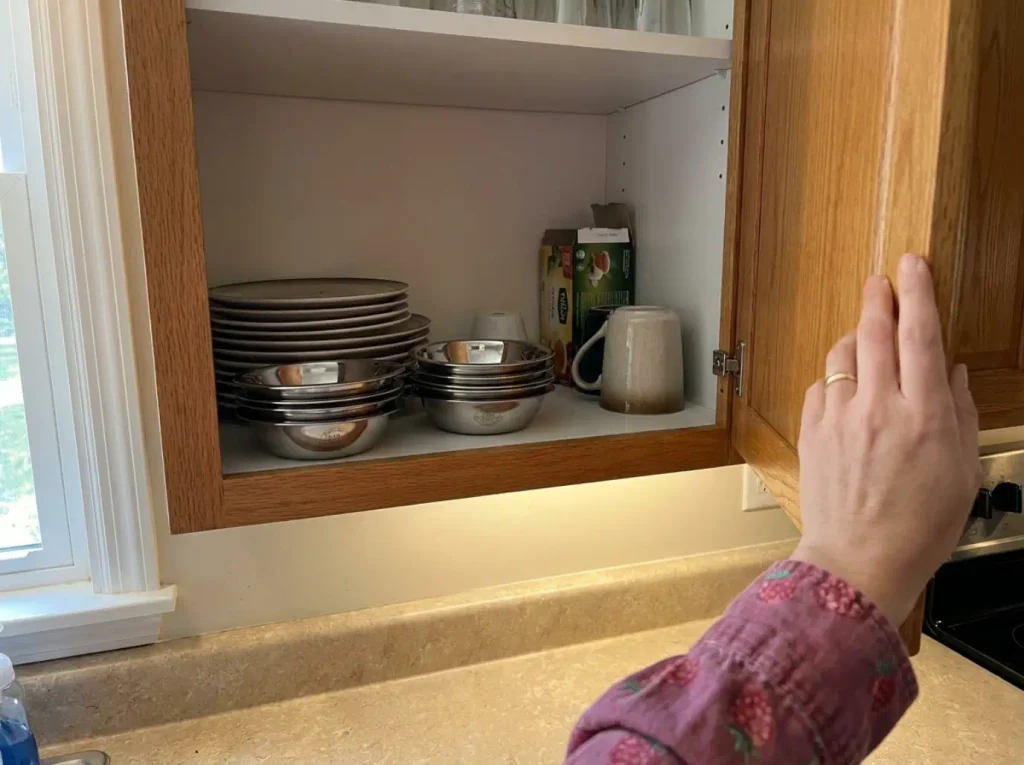 Open kitchen cabinet with a stack of shallow stainless steel cat bowls beside the plates