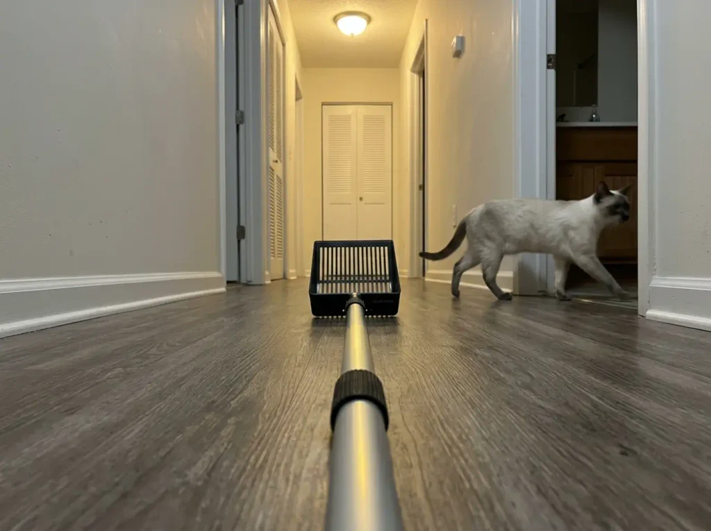 Adjustable long-handled litter scoop on a hallway floor, twist-lock collar visible