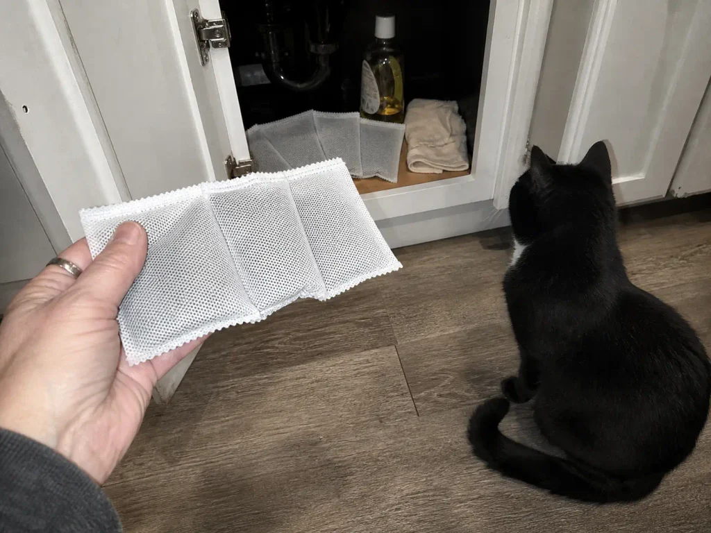 Activated charcoal pouches held in a hand beside the litter box in a bathroom