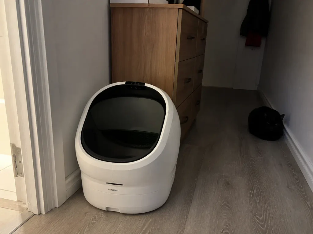 Open-top automatic litter box wedged into a narrow gap beside a bathroom doorway
