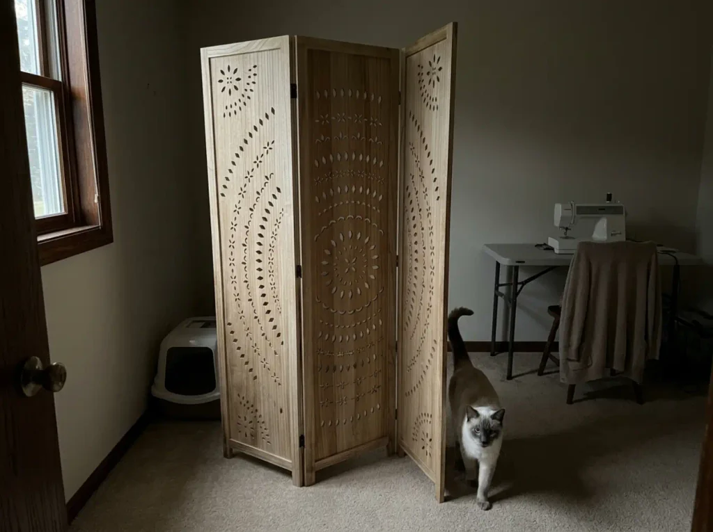 Three-panel folding privacy screen angled around a litter box in the corner of a spare bedroom