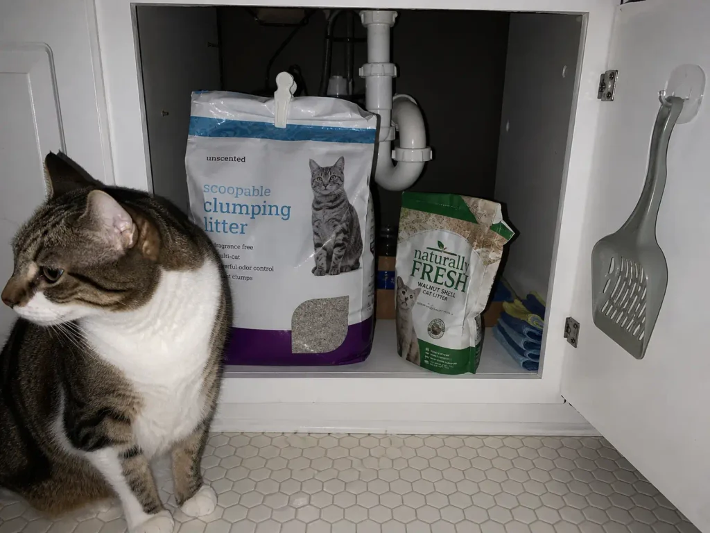 Open under-sink cabinet holding the new litter bag with a small part-used bag of the old litter kept beside it