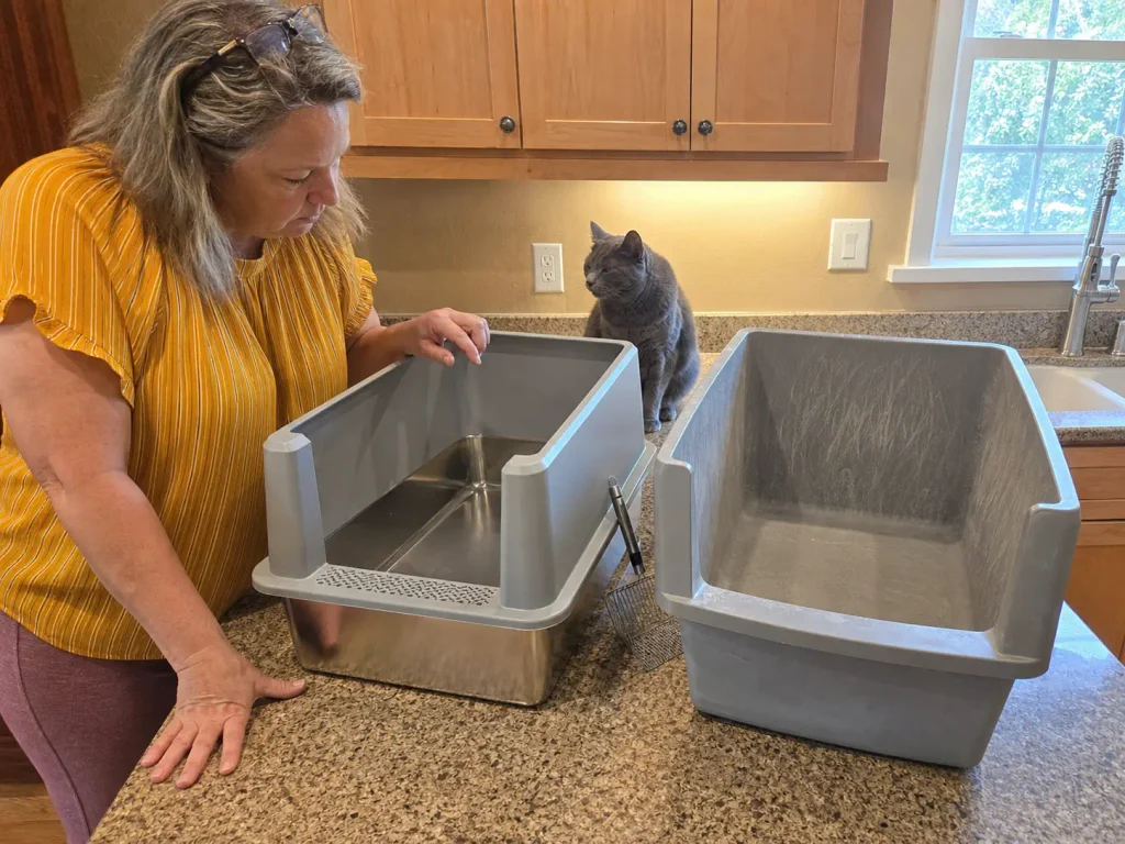 Stainless steel litter box on a kitchen counter beside a scratched plastic one being replaced